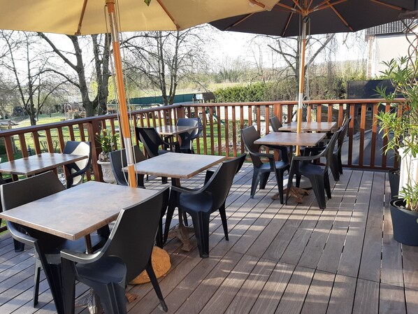 Une terrasse extérieure avec des tables et des chaises en bois, entourée d’une plateforme en bois et d’une petite clôture.