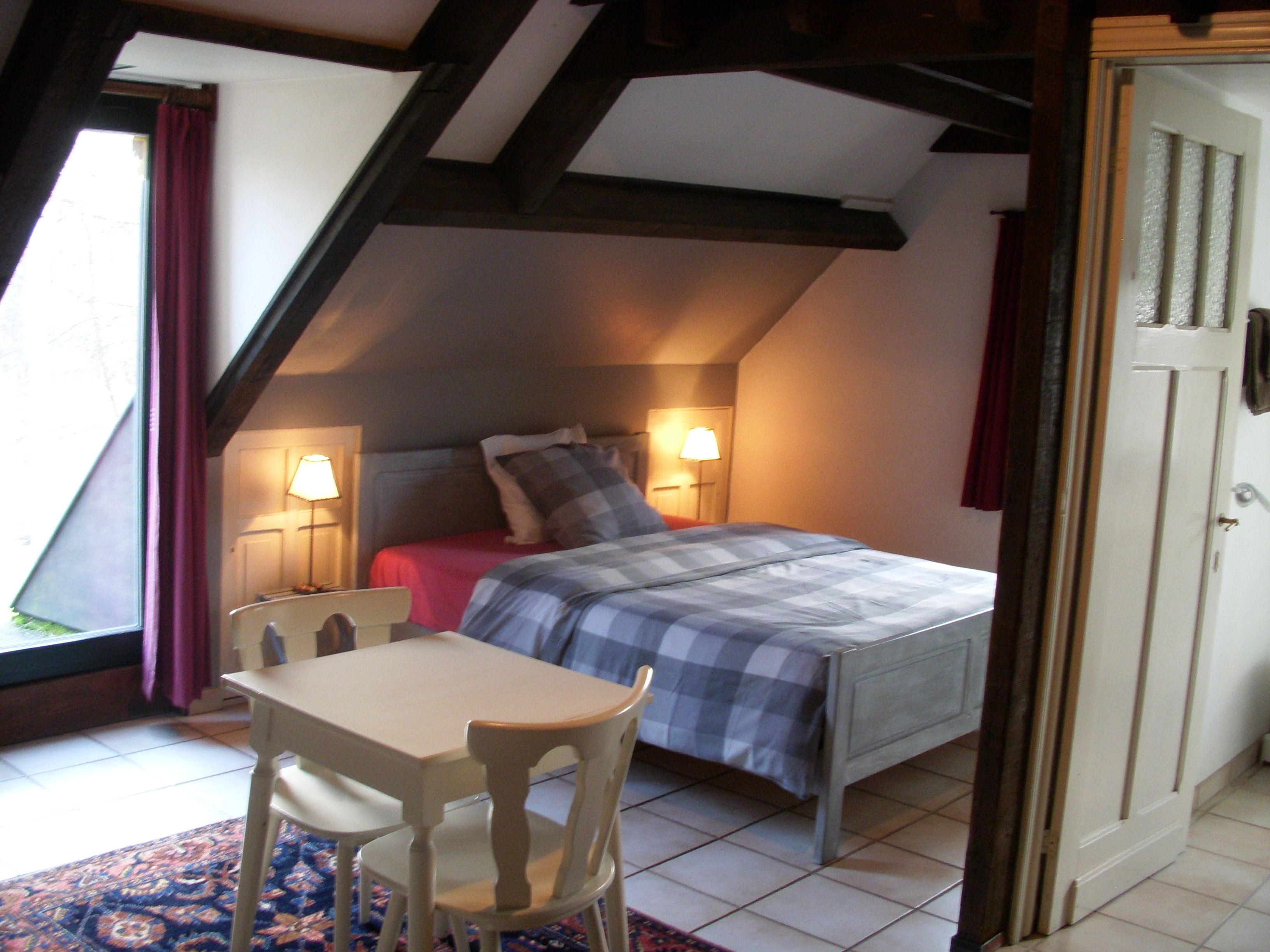 A bedroom with a bed, two bedside lamps, a table with chairs, and a window with curtains.