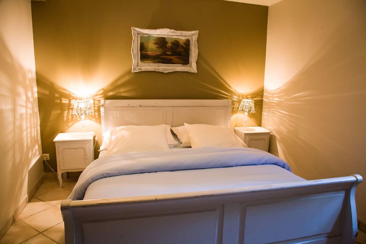 Une chambre à coucher avec un lit blanc, deux tables de chevet avec des lampes, un tableau encadré au mur et un mur vert.