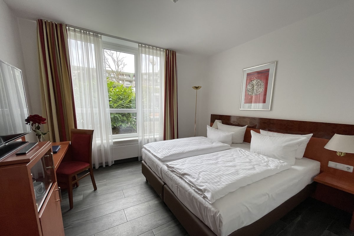A hotel room with two beds, a desk with a computer, a chair, and a window with curtains.