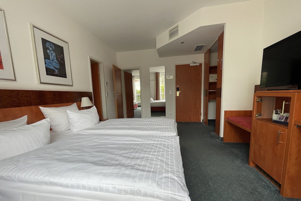A hotel room with two beds, a TV, a wardrobe, and a bathroom visible through an open door.