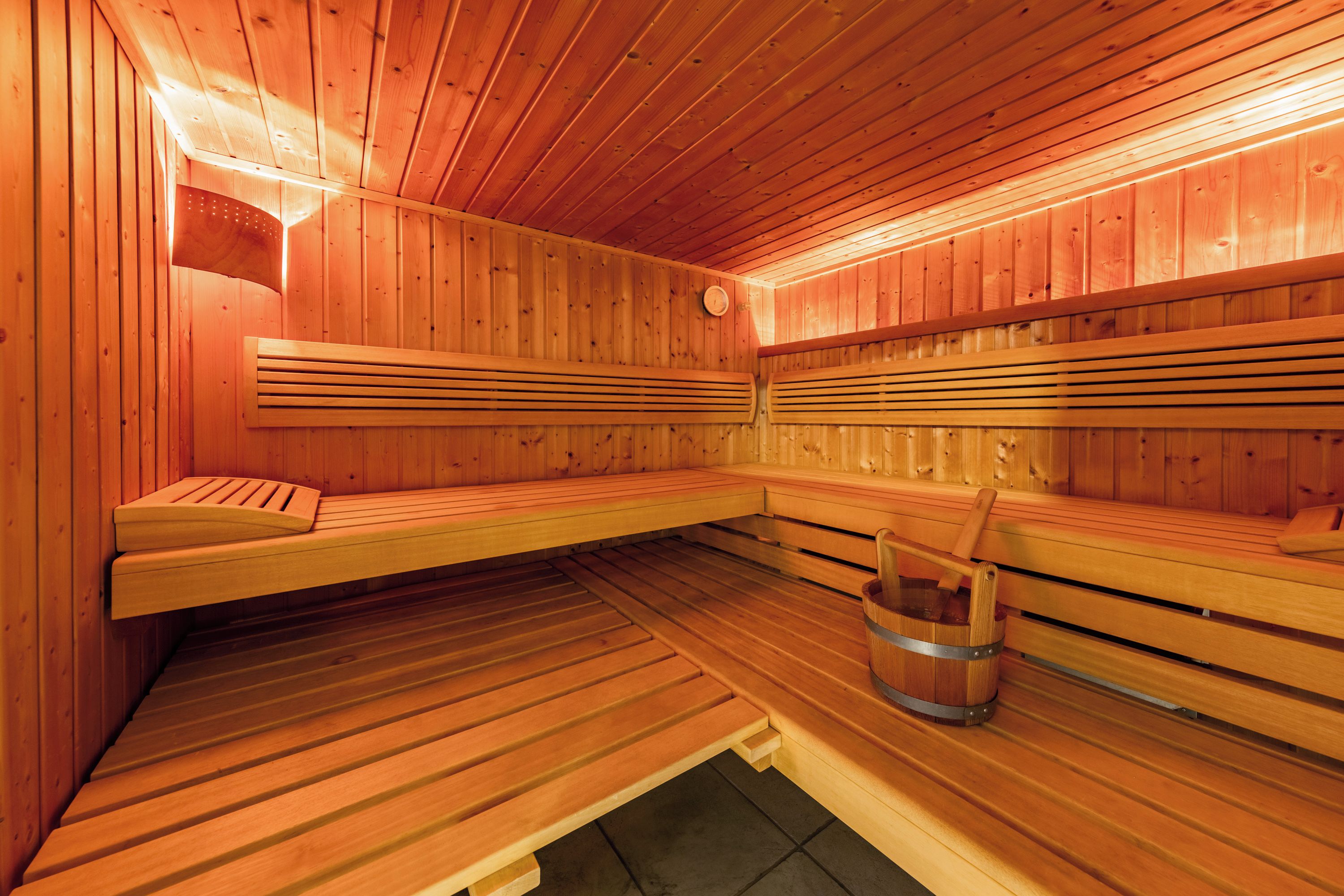 Un sauna avec des bancs en bois, un seau et un radiateur fixé au mur.