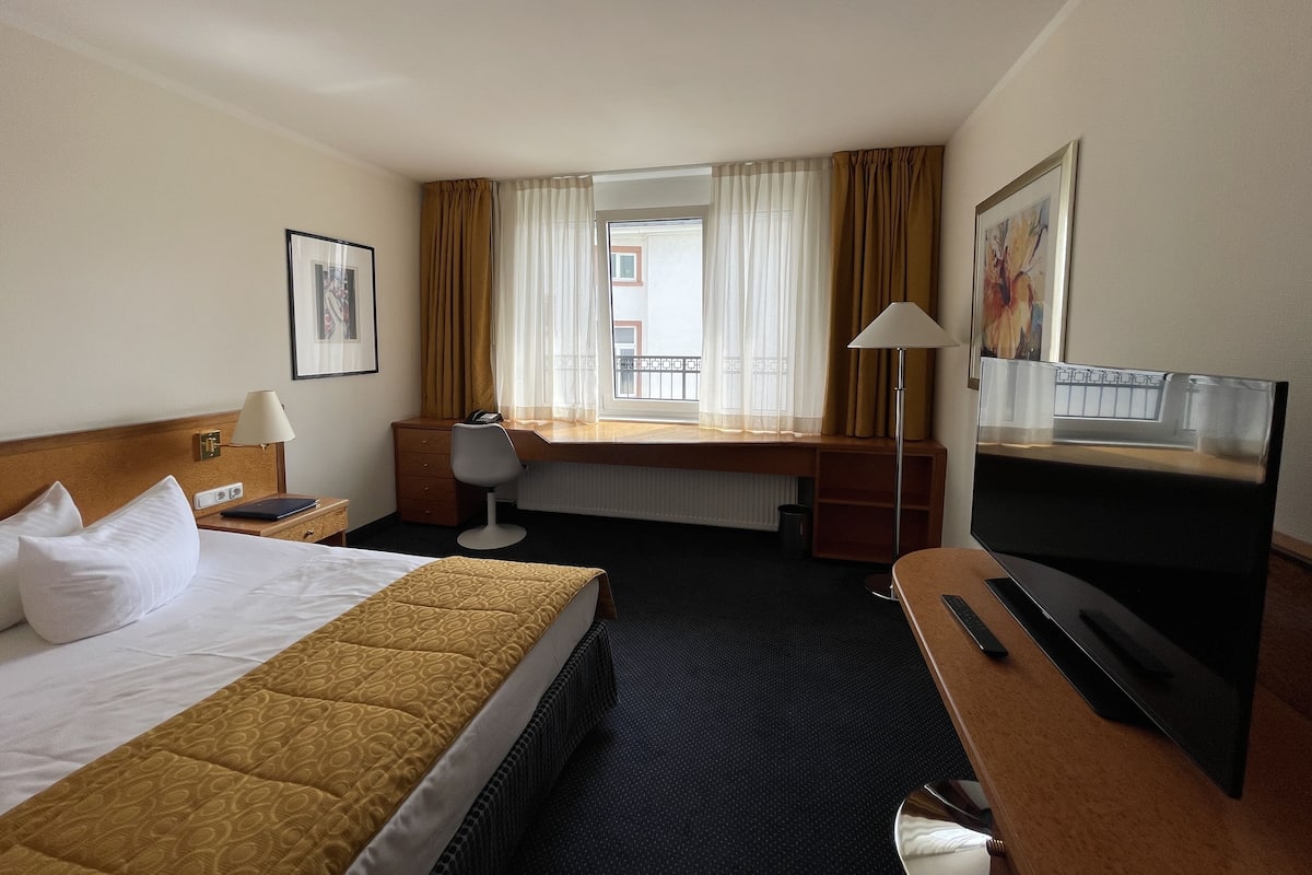 A hotel room with a bed, desk, chair, TV, and a window with curtains.