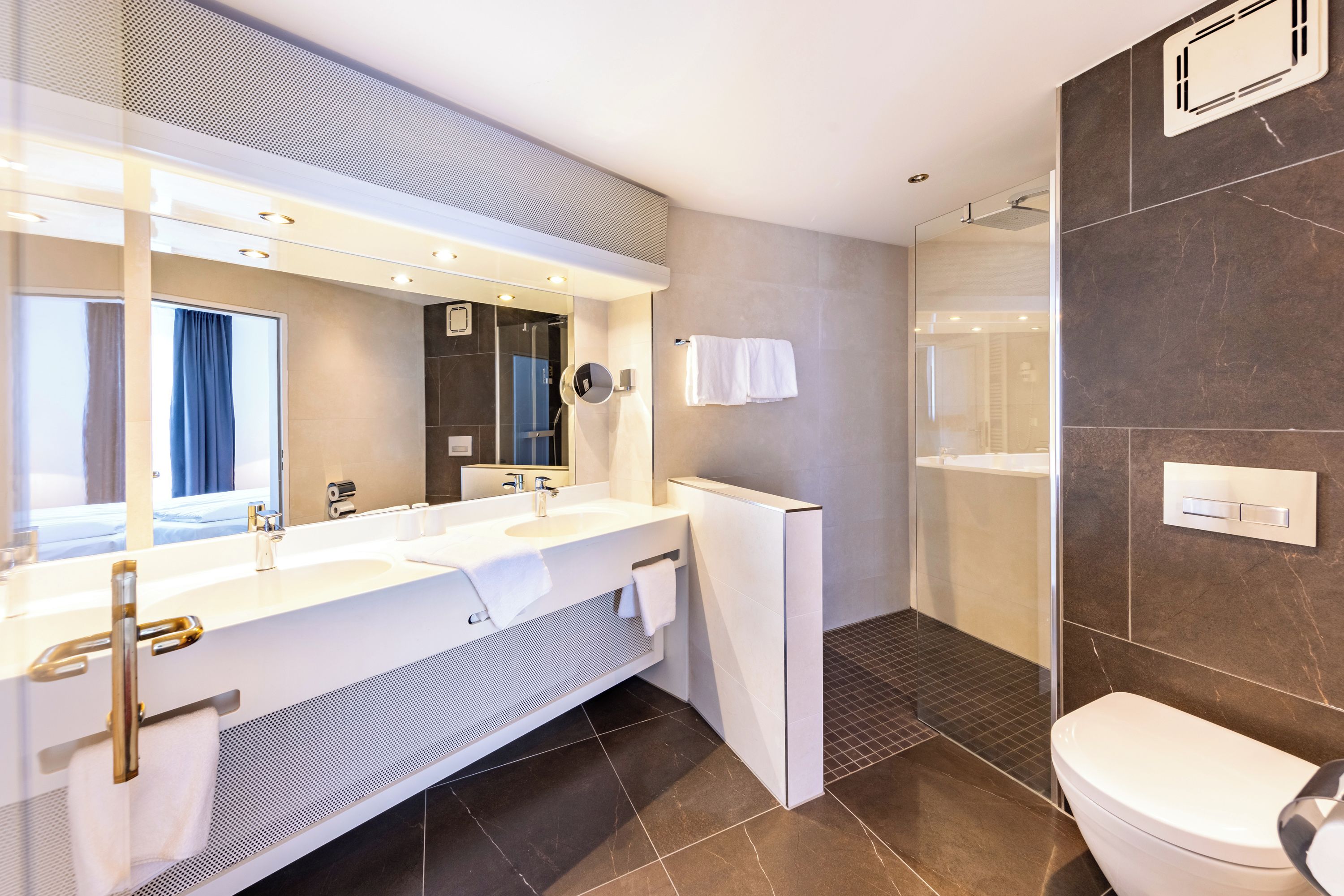 Une salle de bain moderne avec un meuble-lavabo à deux vasques, un grand miroir, des toilettes et un espace douche.
