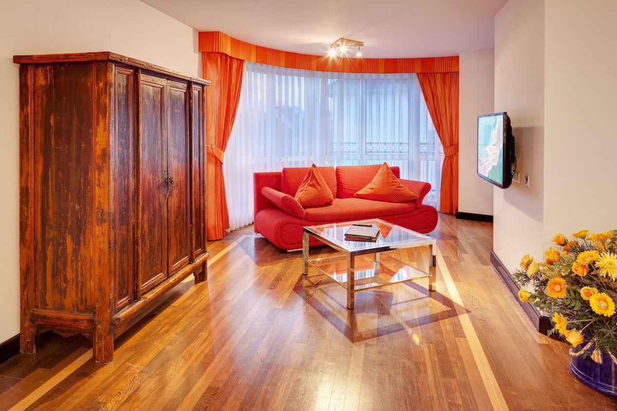 A living room with a red sofa, a wooden cabinet, a glass coffee table, and a TV on the wall.