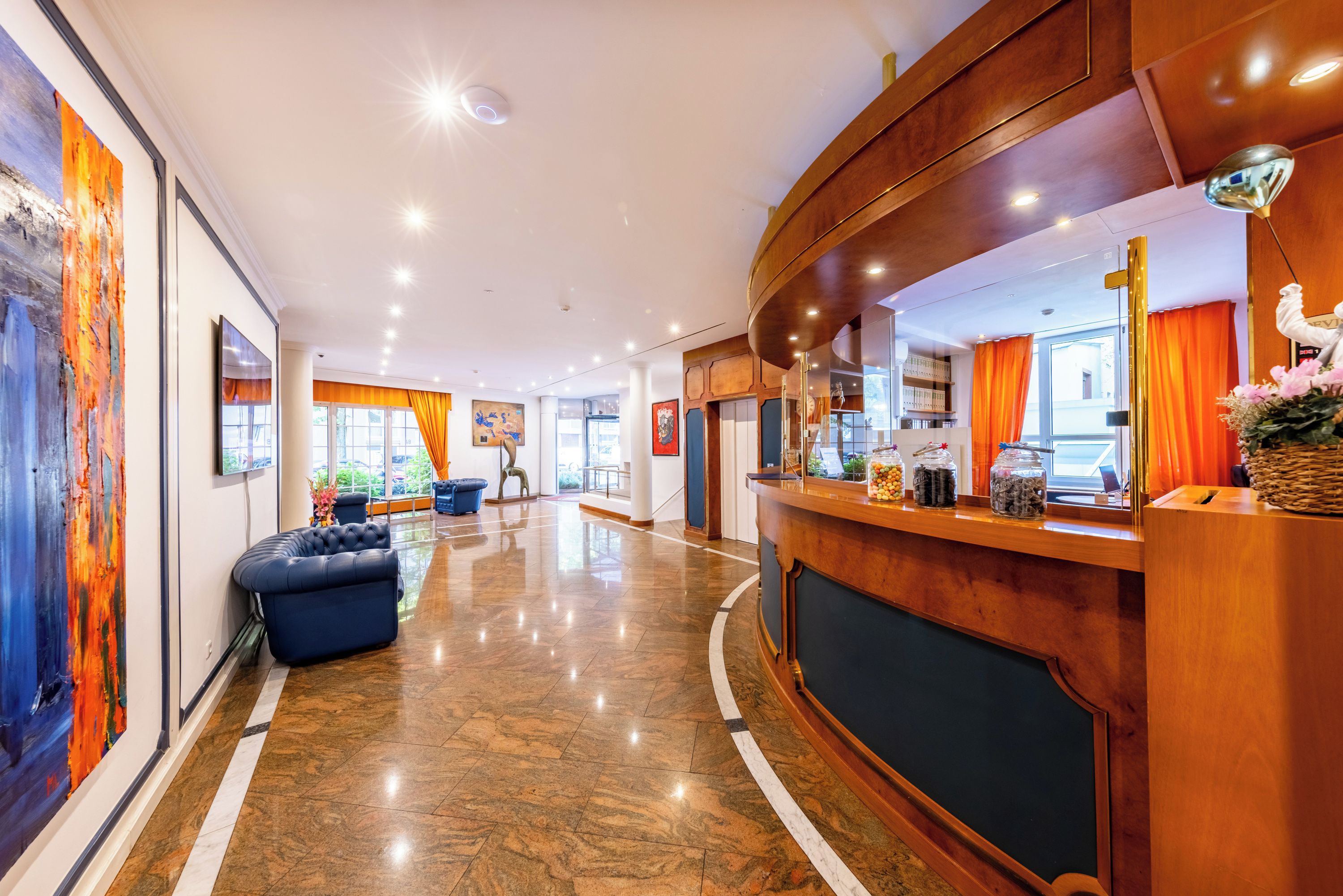 Eine Hotelhalle mit Empfangstresen, Sitzgelegenheiten und Kunstwerken an den Wänden.