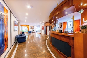 Een hotel lobby met een receptiebalie, een zithoek en kunstwerken aan de wanden.