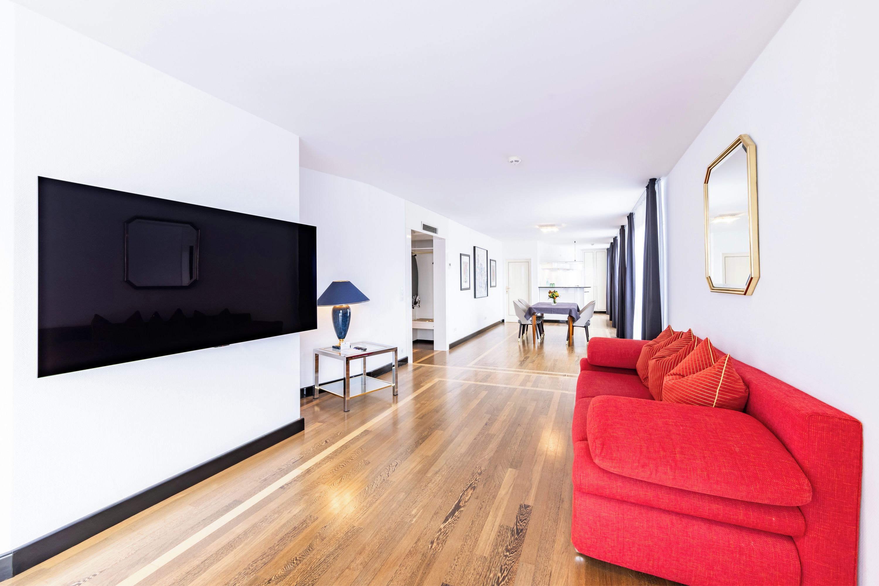 Ein modernes Interieur mit einem roten Sofa, einem an der Wand montierten Fernseher und einer Essecke mit Tisch und Stühlen.