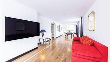 Ein modernes Interieur mit einem roten Sofa, einem an der Wand montierten Fernseher und einer Essecke mit Tisch und Stühlen.