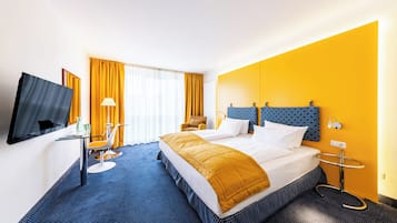 Ein Hotelzimmer mit einem großen Bett, einem Schreibtisch mit Stuhl, einem Fernseher und einem Fenster mit Vorhängen.