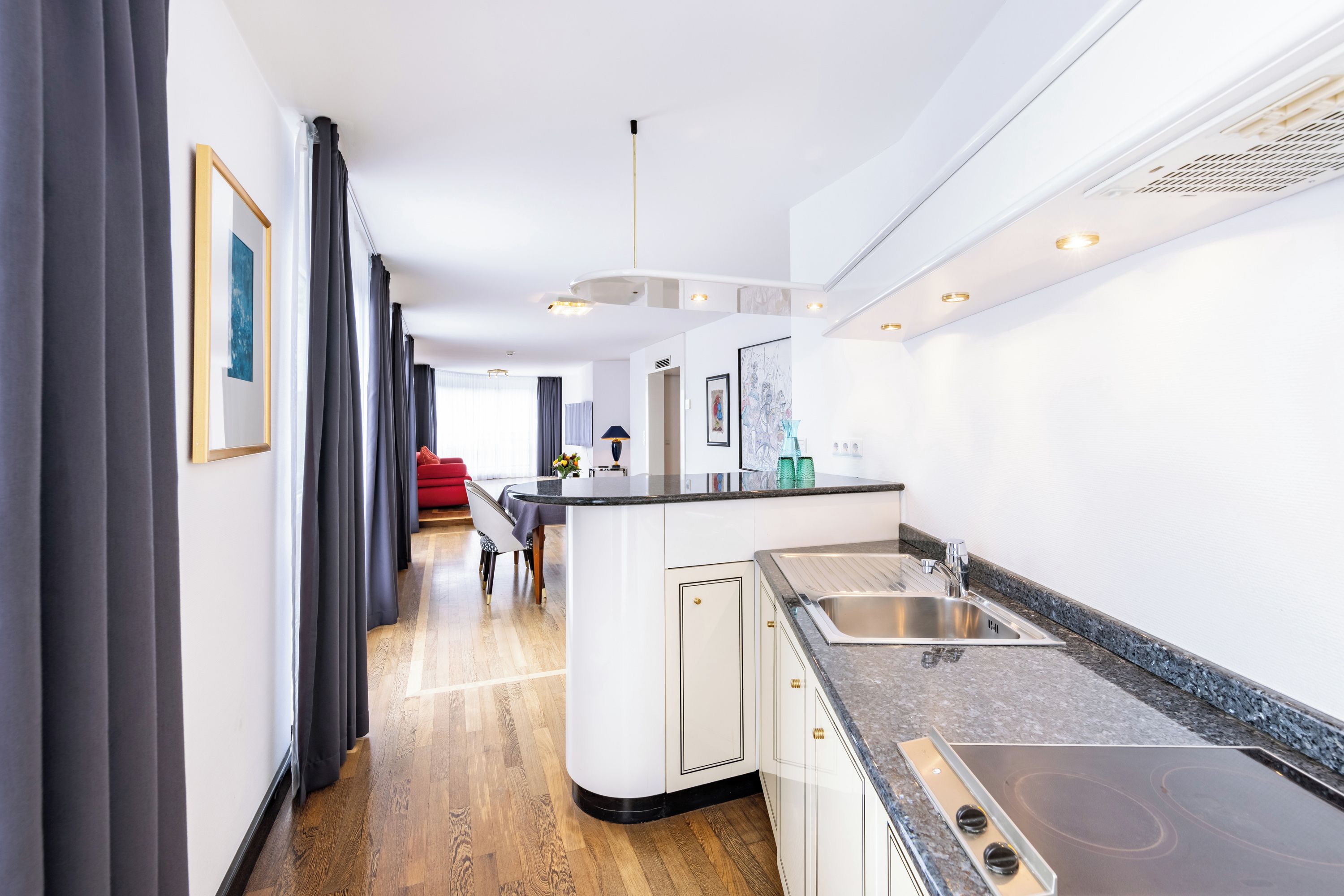 Cocina moderna con una isla central, electrodomésticos integrados y un comedor con una silla roja.