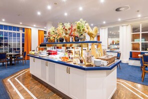 Een ontbijtbuffet in een hotel met diverse soorten eten en een decoratieve haanbeeld.