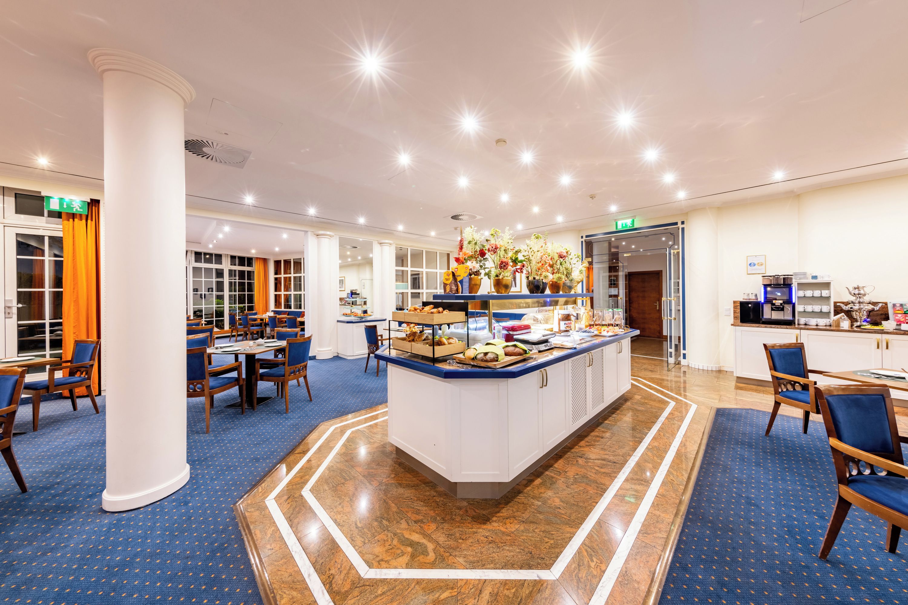 Ein Hotel-Speisesaal mit einem zentralen Buffet, verschiedenen Sitzgelegenheiten und einem modernen Innenraum.
