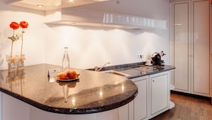 A modern kitchen with a curved granite countertop, a built-in sink, and white cabinetry. There are two red roses in glass vases on the countertop. - Hotel Alexander am Zoo (Frankfurt)