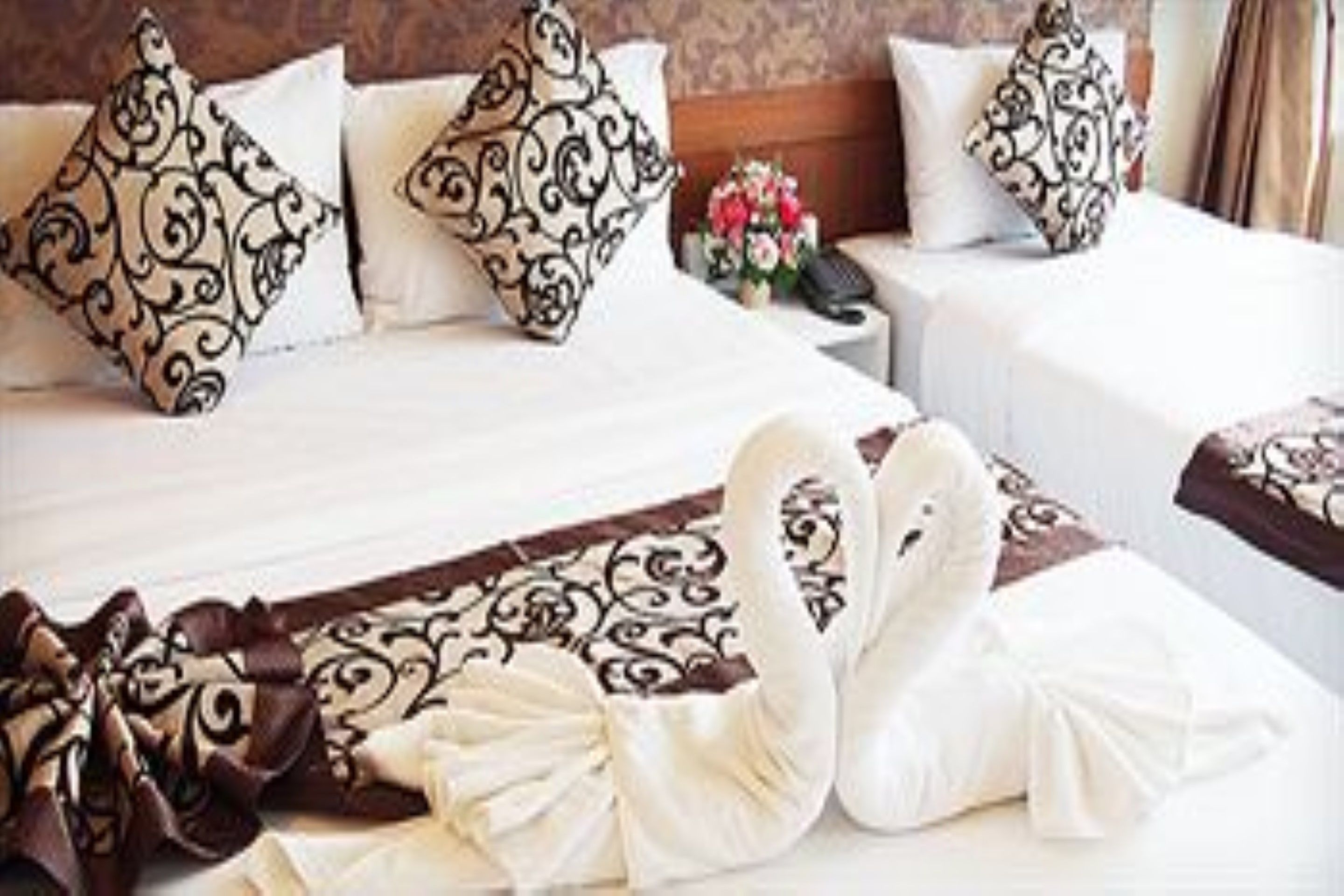 A hotel room with two beds, ornate pillows, a bouquet of flowers, and a swan-shaped decoration.