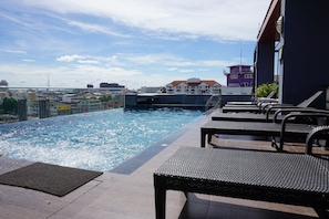 An outdoor swimming pool with lounge chairs, a view of the cityscape, and a building with a purple facade in the background.