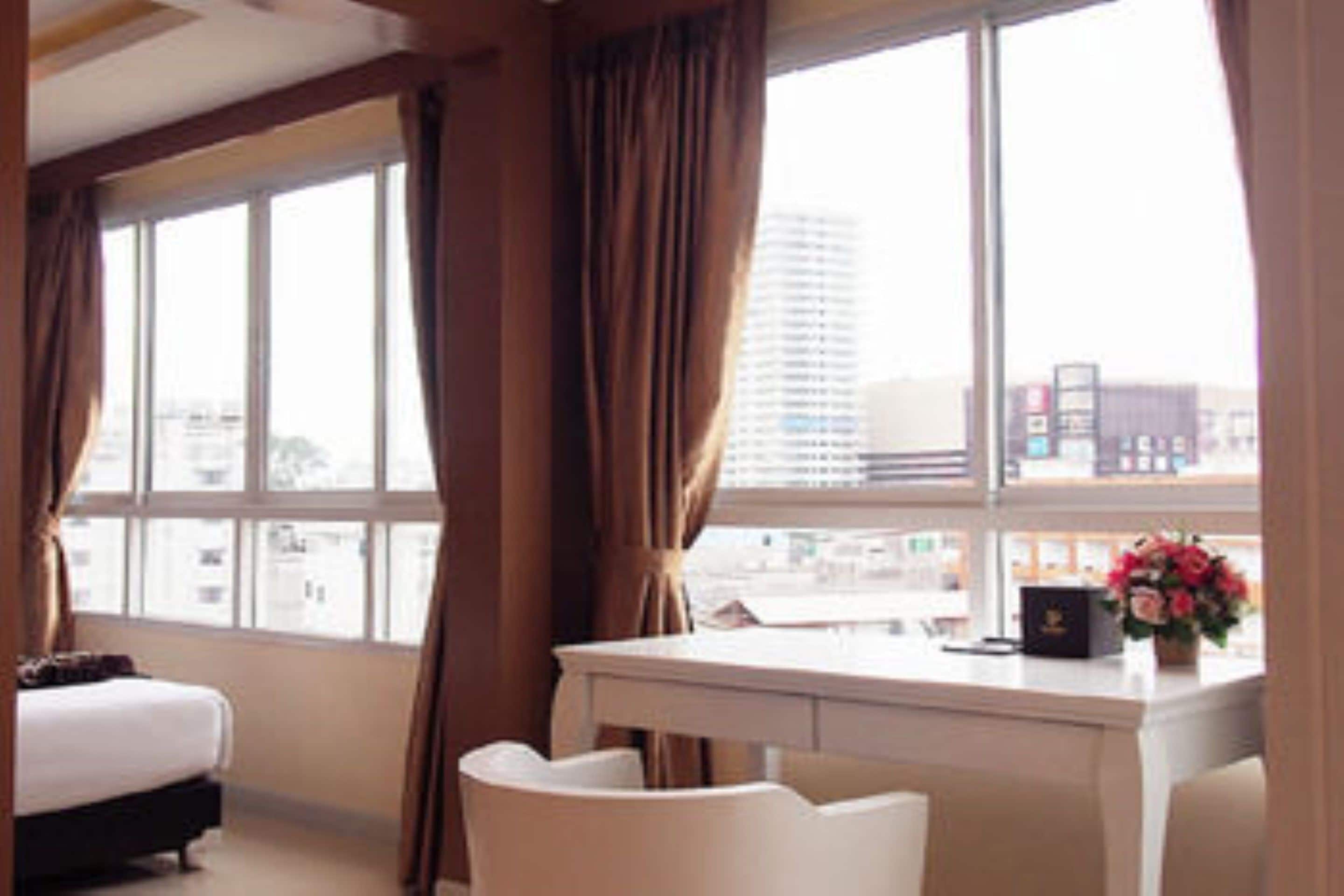 Habitación de hotel con cama, escritorio y silla. Cuenta con ventana con cortinas y vistas a edificios.