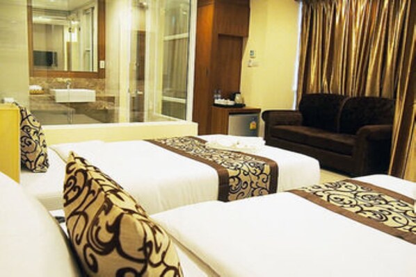 Quarto de hotel com duas camas, um sofá, uma mesa pequena e um banheiro visível através de uma porta de vidro.