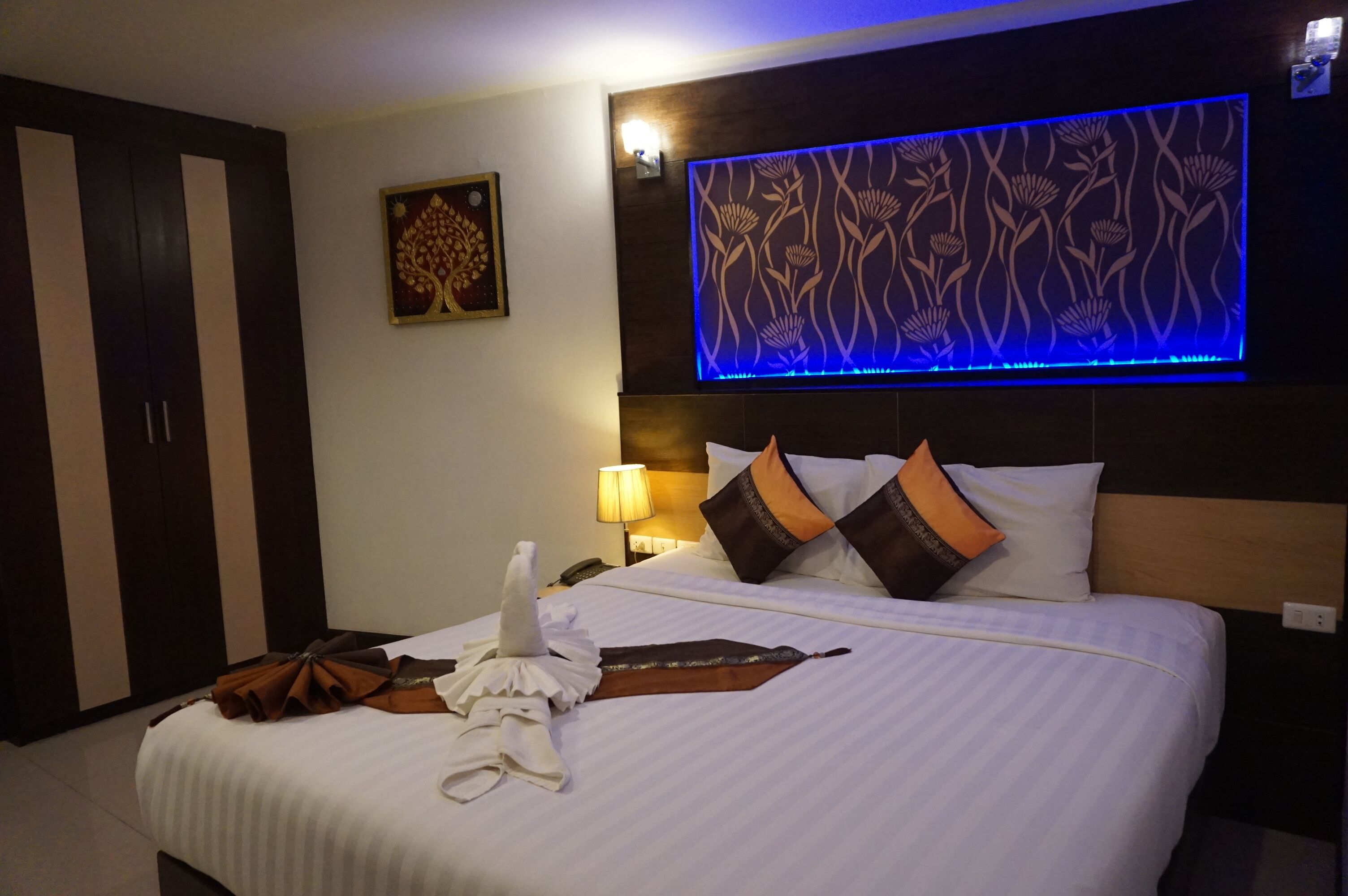 A hotel room with a bed, a wall-mounted TV, a nightstand, a lamp, and a wardrobe.