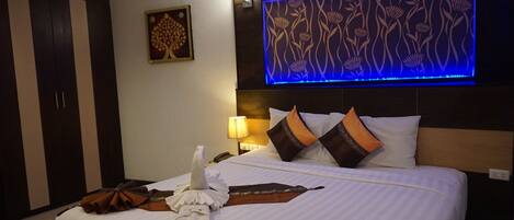 A hotel room with a bed, a wall-mounted TV, a nightstand, a lamp, and a wardrobe.