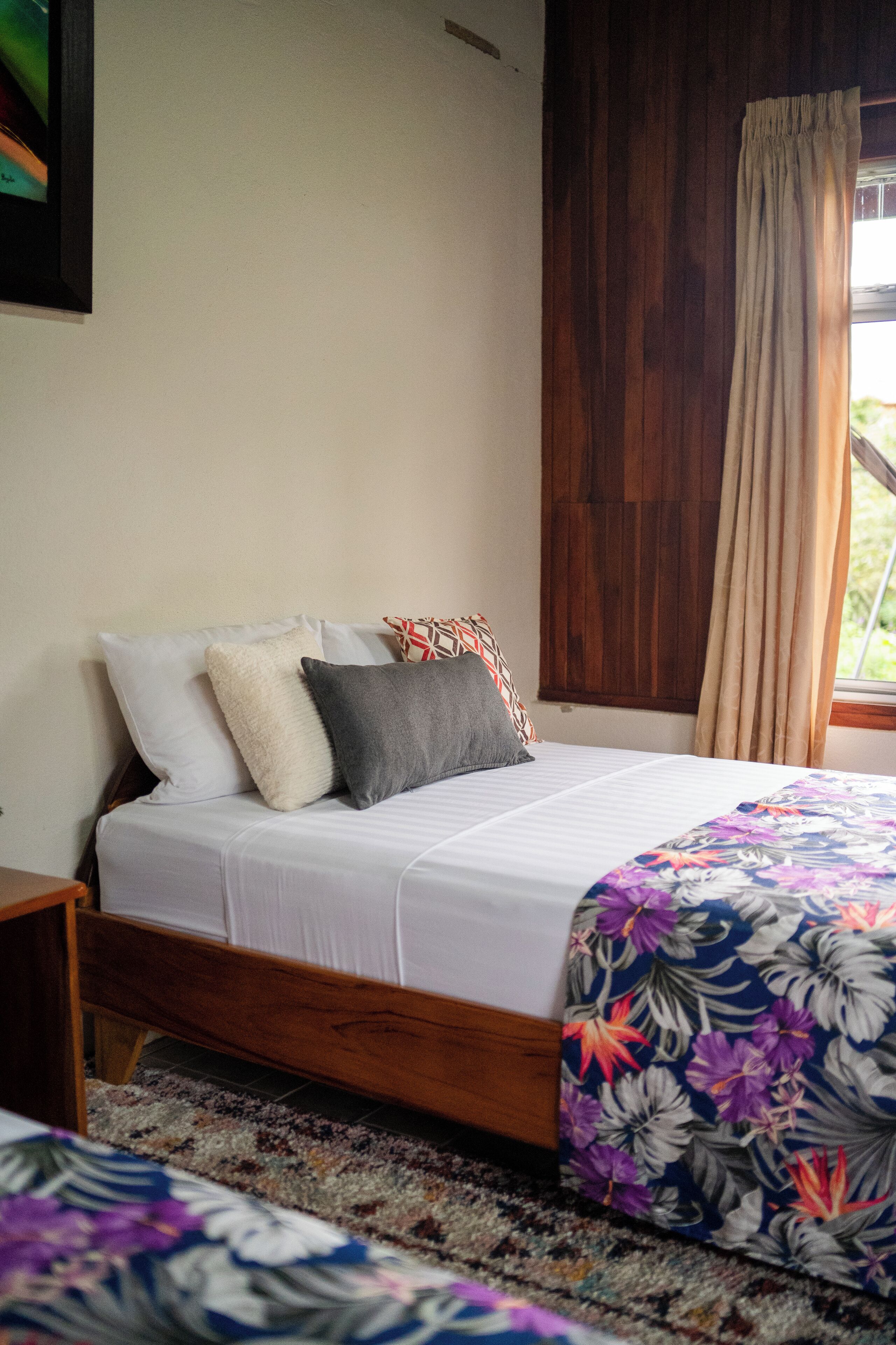 A bedroom with a wooden bed frame, white bedding, and a floral-patterned bedspread.