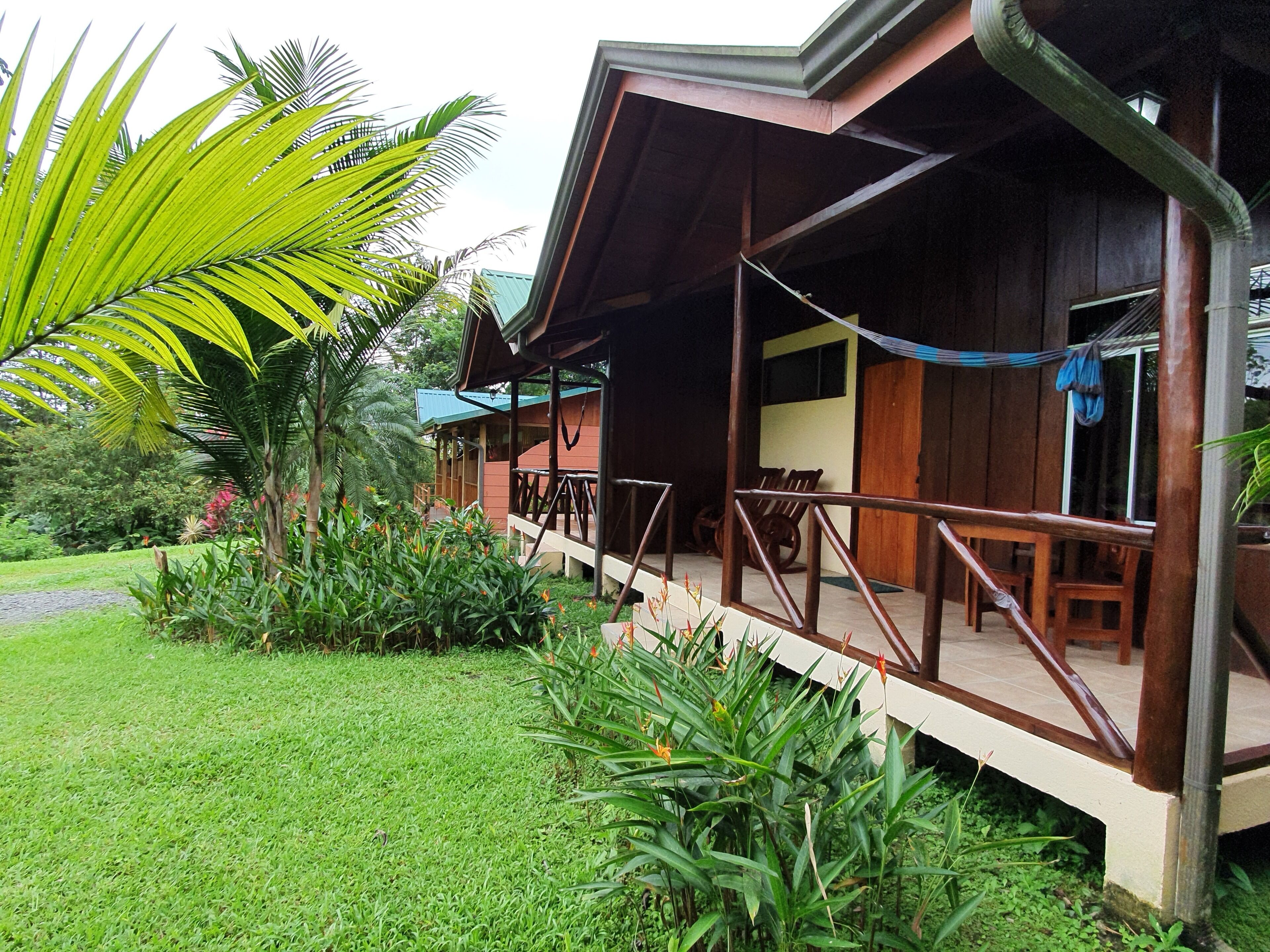 A wooden building with a porch, surrounded by lush greenery and a well-maintained lawn.