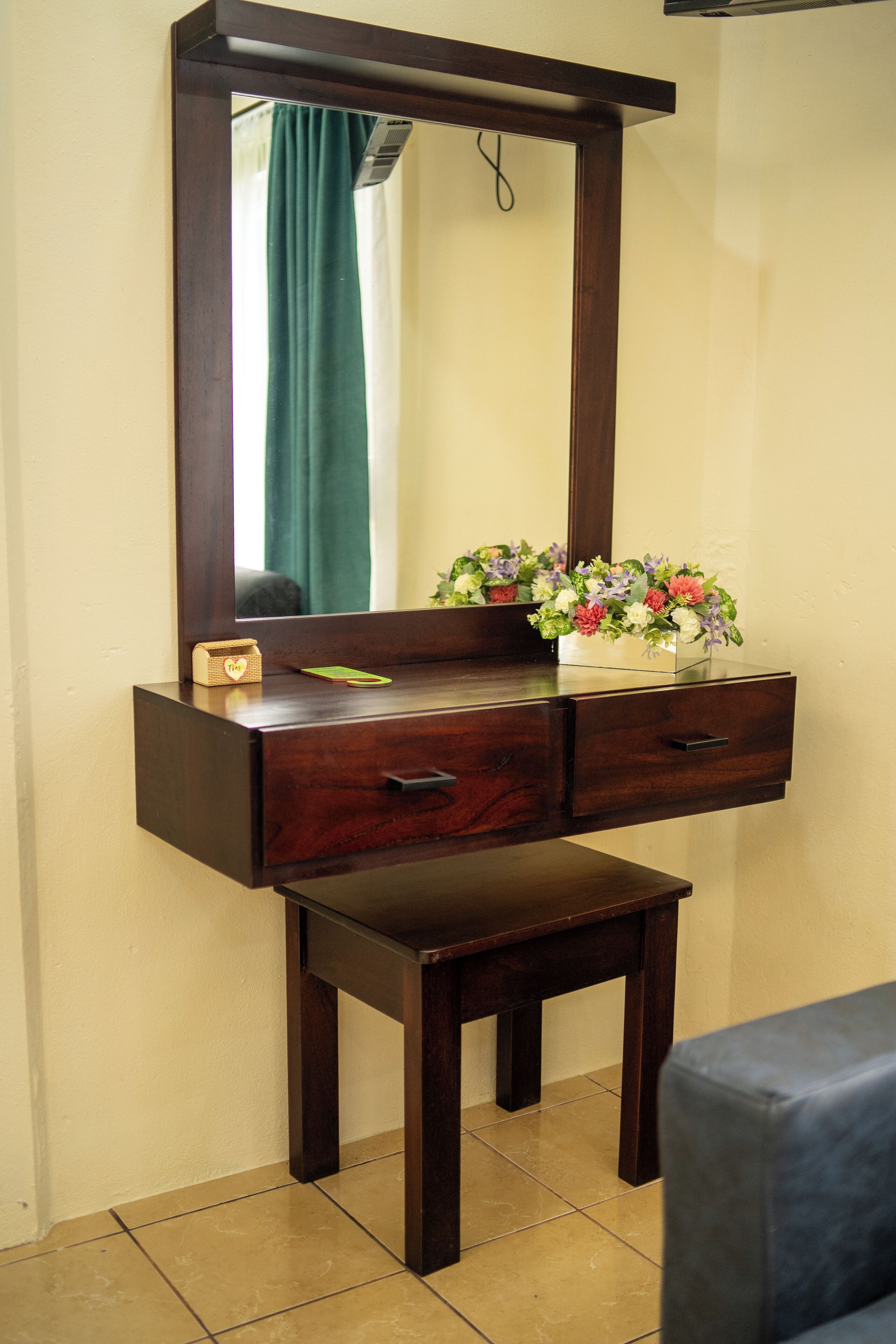 A wooden dresser with a mirror, a small stool, and a floral arrangement.