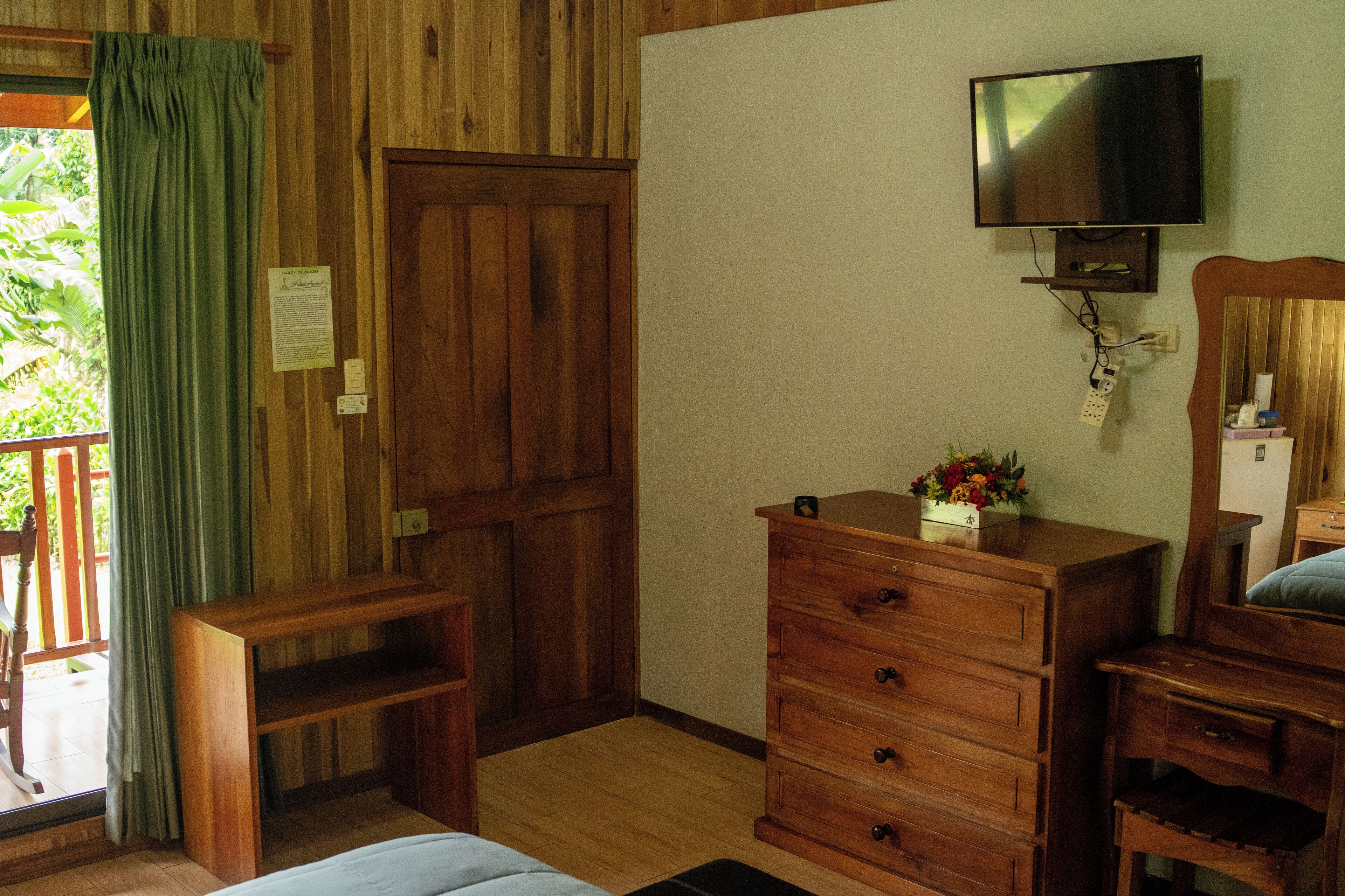 A wooden room with a wooden dresser, a television mounted on the wall, and a door with a green curtain.