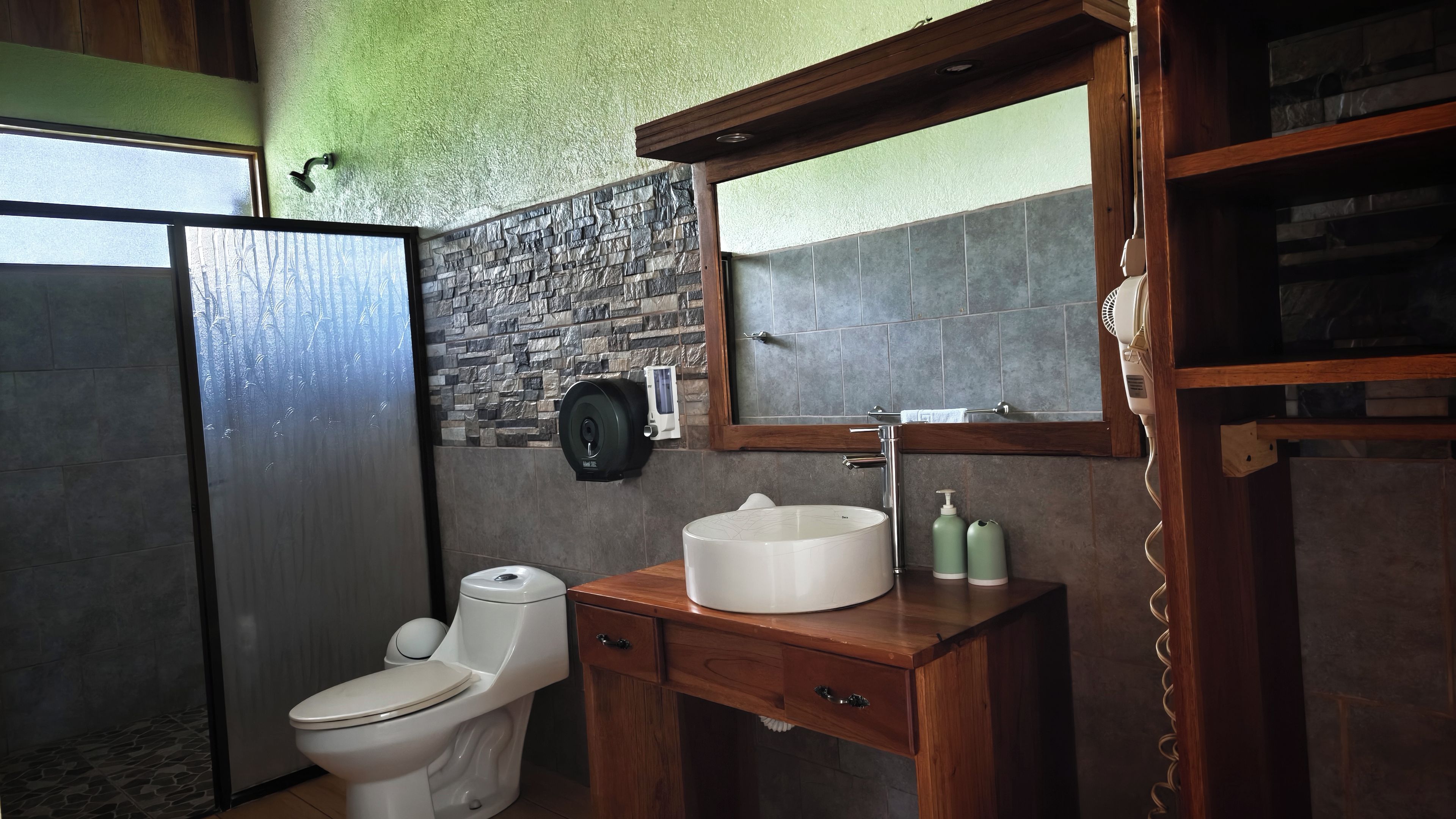 A bathroom with a toilet, a sink with a mirror, and a shower area.