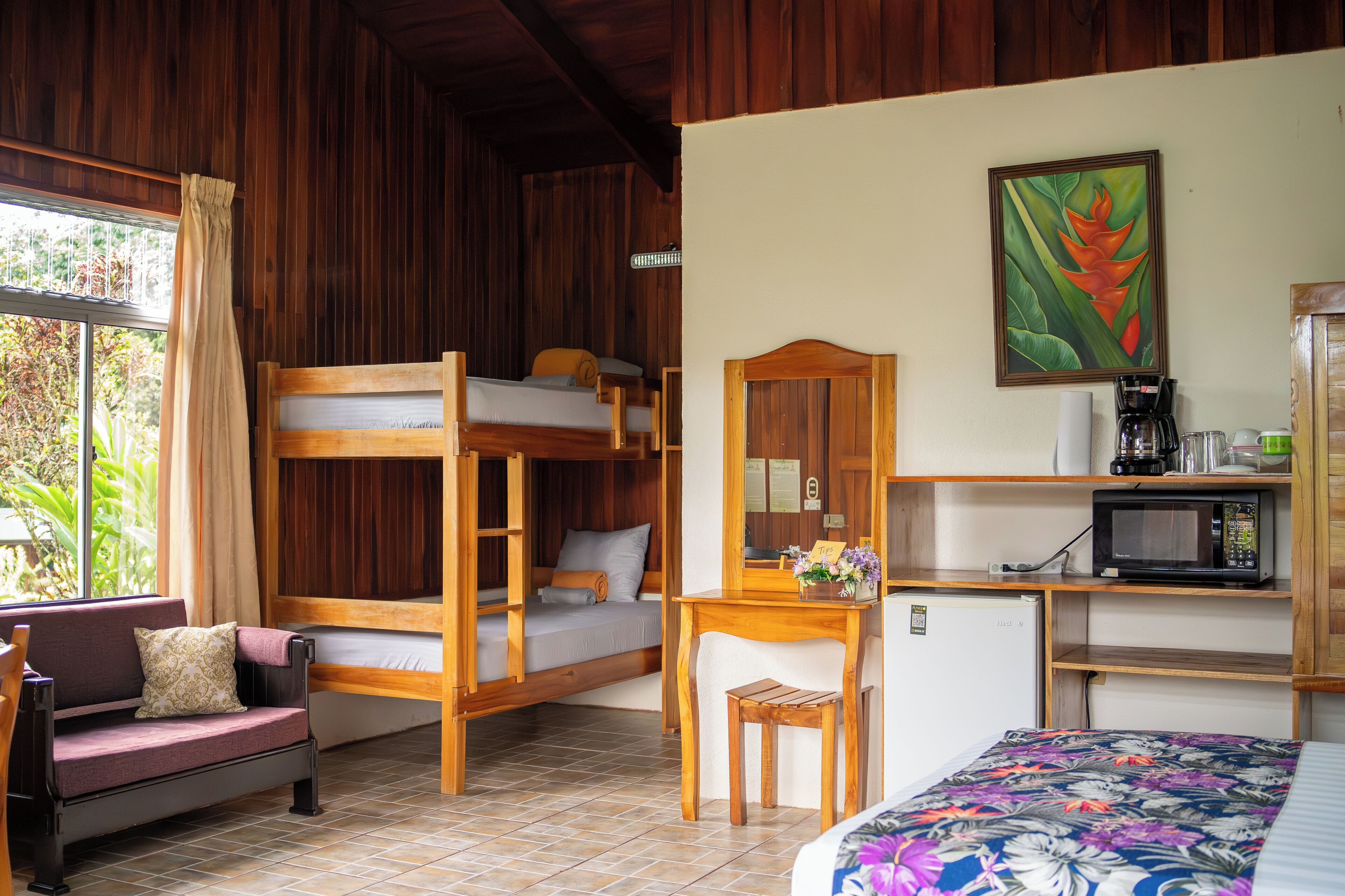 Une chambre avec un lit superposé, un bureau avec une chaise, un petit réfrigérateur, un four à micro-ondes et une fenêtre avec des rideaux.