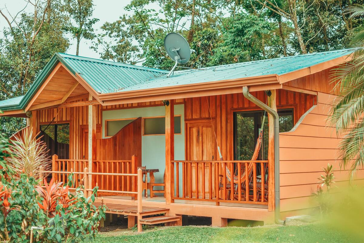 A wooden cabin with a porch, a satellite dish, and a view of the surrounding greenery.