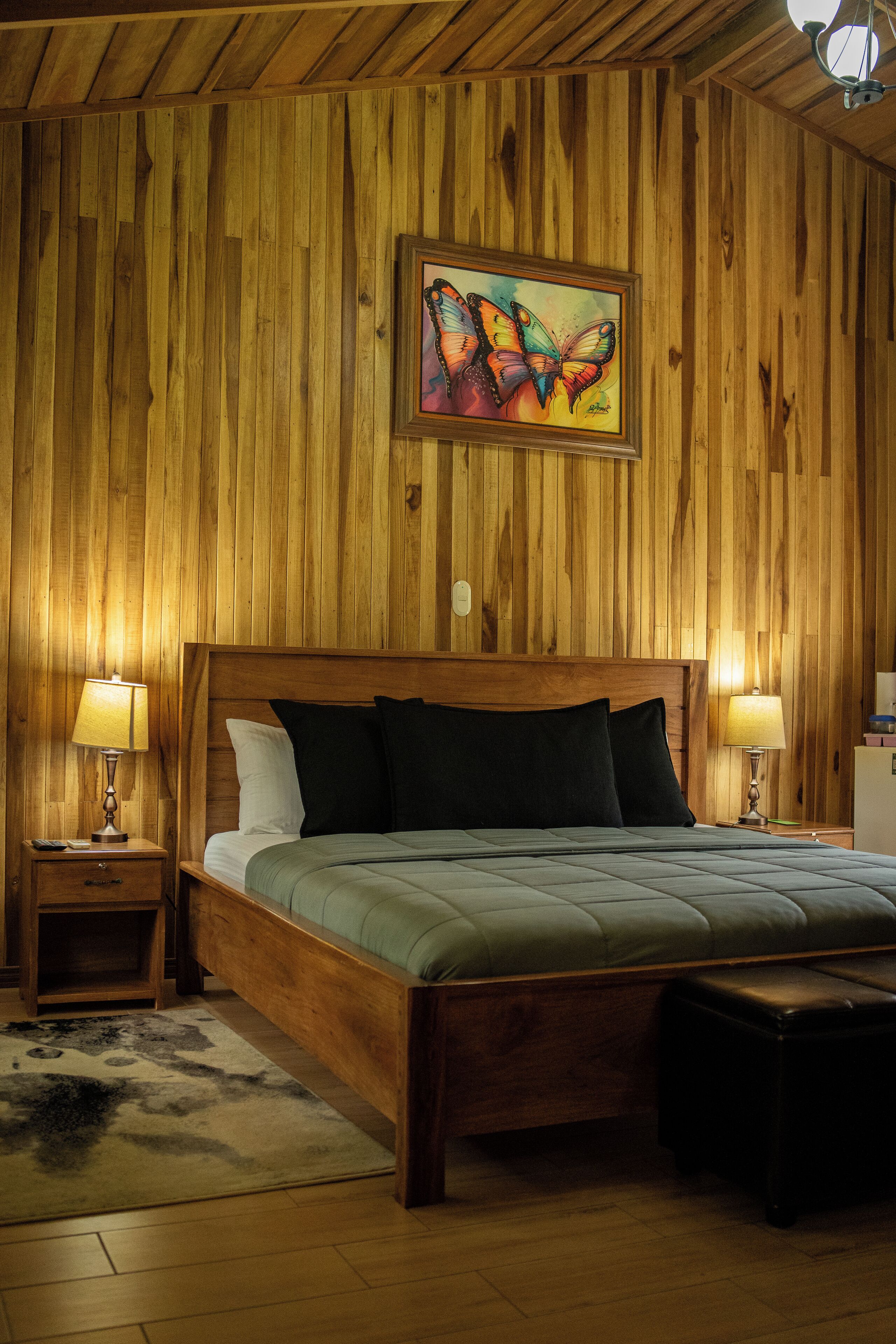 Une chambre à coucher aux murs lambrissés, avec un lit, deux lampes de chevet, une table de chevet, un tapis et un tableau accroché au mur.
