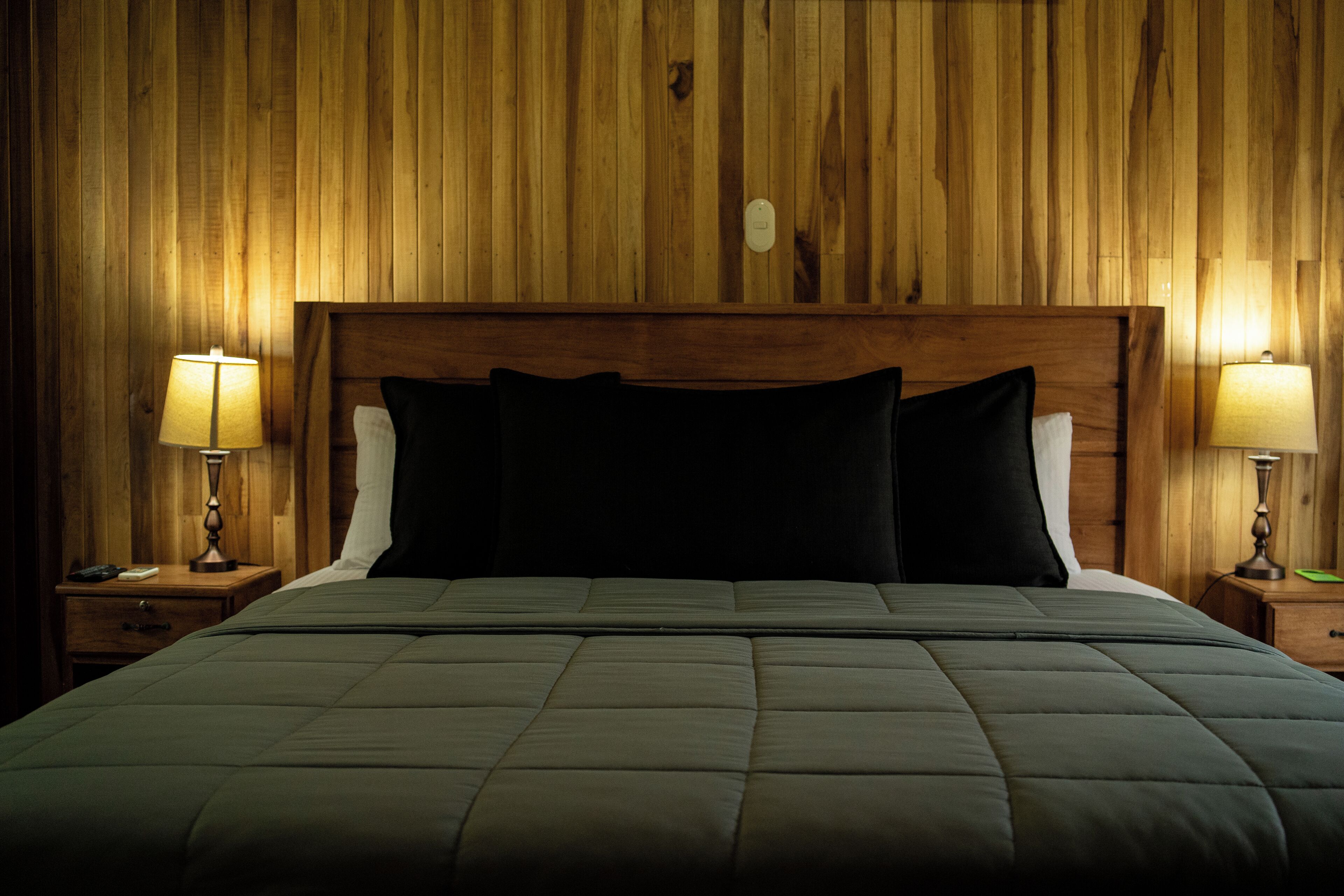 A bed with a wooden headboard, two bedside tables with lamps, and a quilted bedspread.