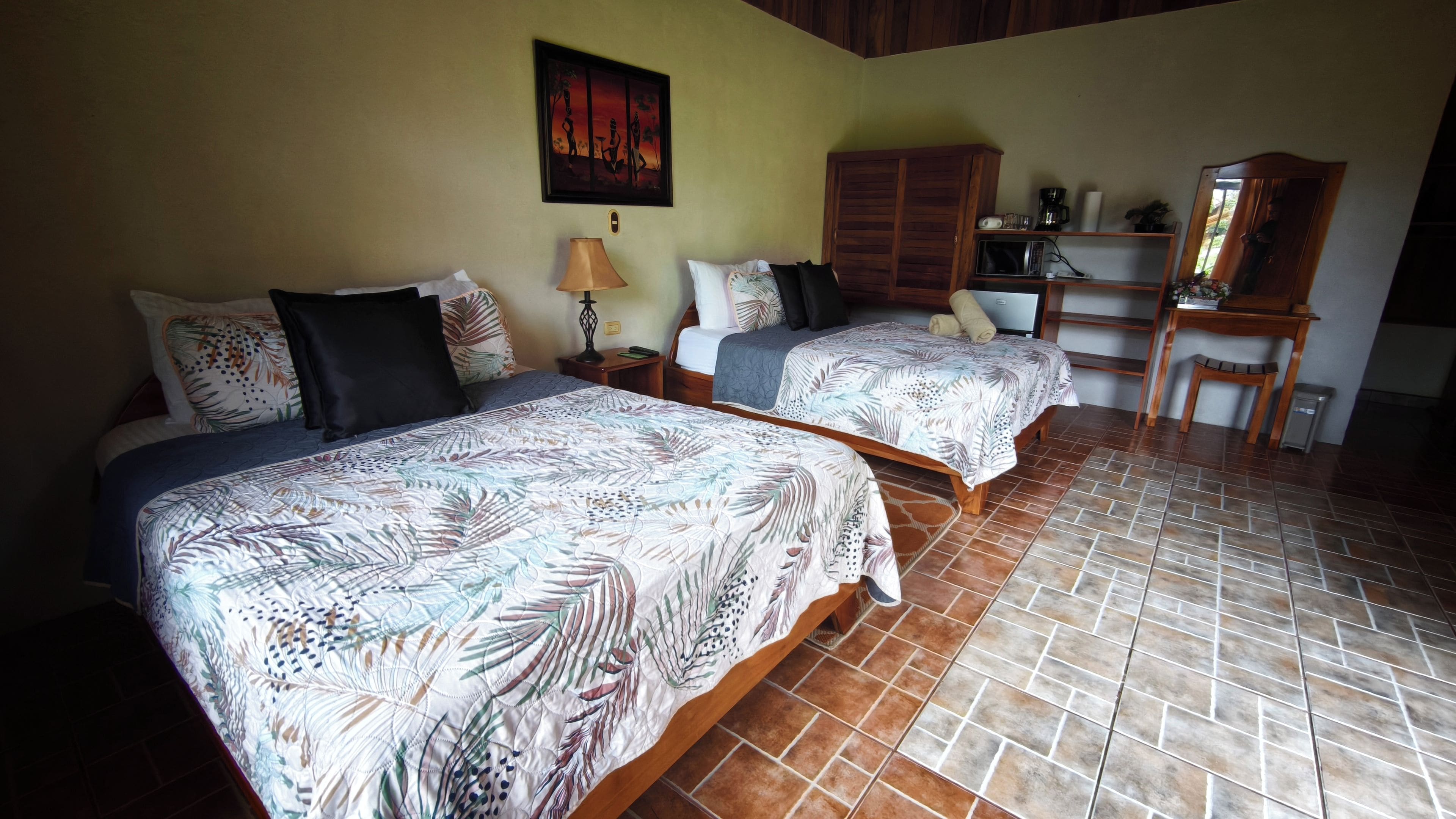 Habitación de hotel con dos camas, un escritorio, una silla, un armario y un cuadro en la pared.