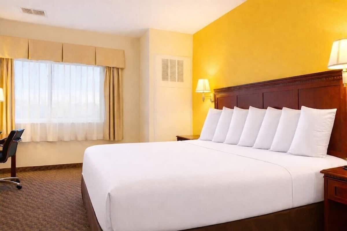 A hotel room with a large bed, a desk, and a window with curtains.