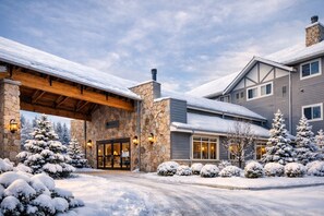 A large stone building with a covered entrance, snow-covered trees, and a clear sky.
