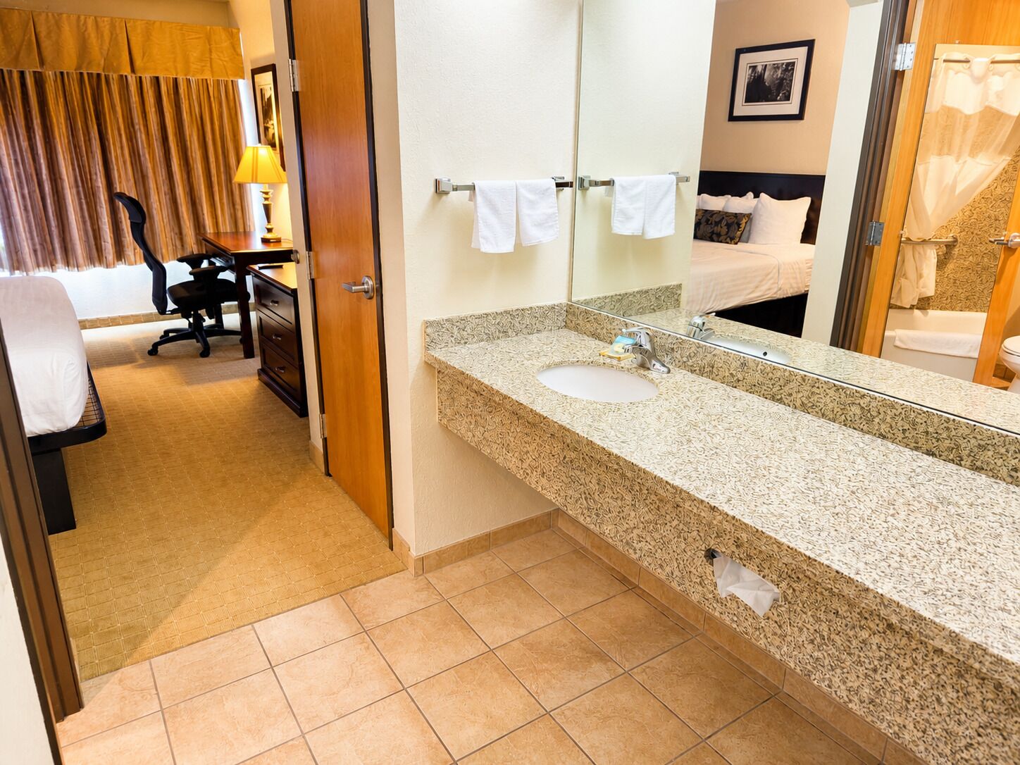 A hotel bathroom with a granite countertop, a sink, a mirror, and a towel rack.