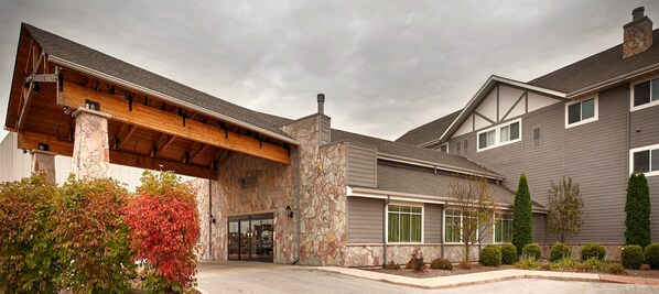 A modern building with a stone facade, a covered entrance, and a well-maintained garden.