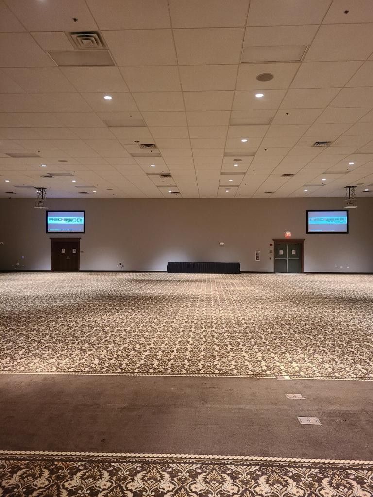 Un salón de conferencias amplio con alfombra estampada, dos pantallas de proyección y un escenario.