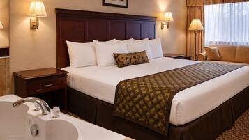 A hotel room with a large bed, a sitting area with a sofa, a desk, a lamp, a picture on the wall, and a bathtub.