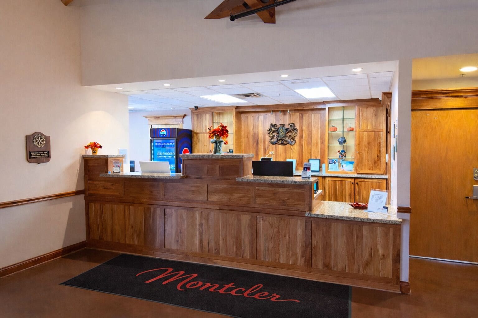 A reception desk with a wooden finish, a digital screen, and a Pepsi refrigerator.