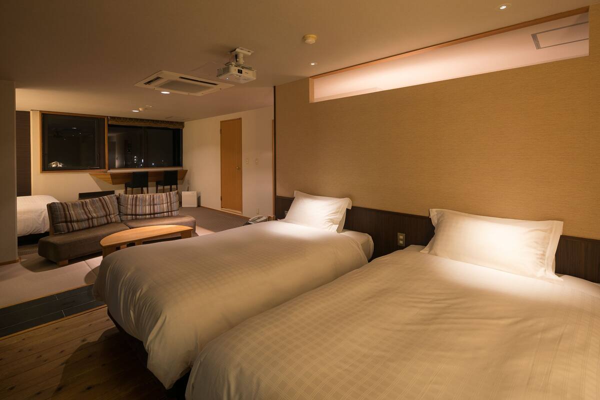 A hotel room with two beds, a sofa, a small table, and a TV.
