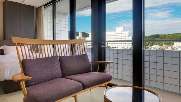 A modern hotel room with a wooden sofa, a small round table, and a bed. - Shimahana (Sumoto)