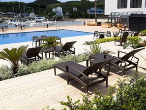 A poolside area with lounge chairs and tables, surrounded by greenery and overlooking a marina. - Shimahana (Sumoto)