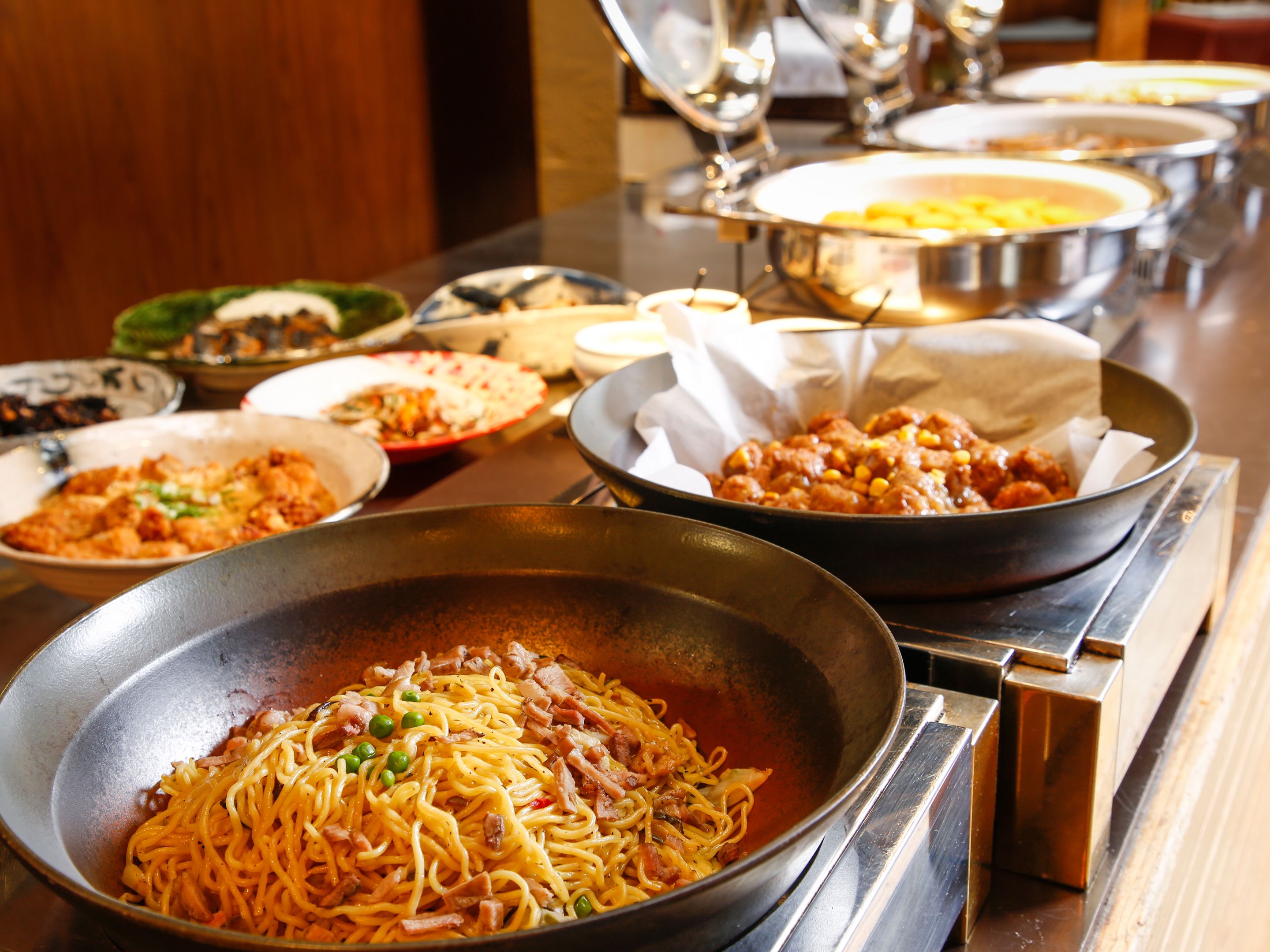 A buffet table with various dishes including noodles, meats, and vegetables.
