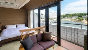 A hotel room with a bed, a sofa, and a view of a river and buildings. - Shimahana (Sumoto)