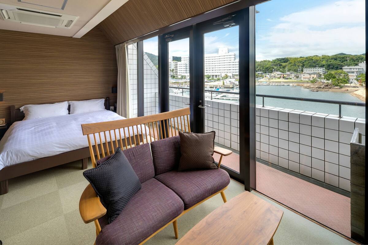 A hotel room with a bed, a sofa, and a view of a river and buildings.