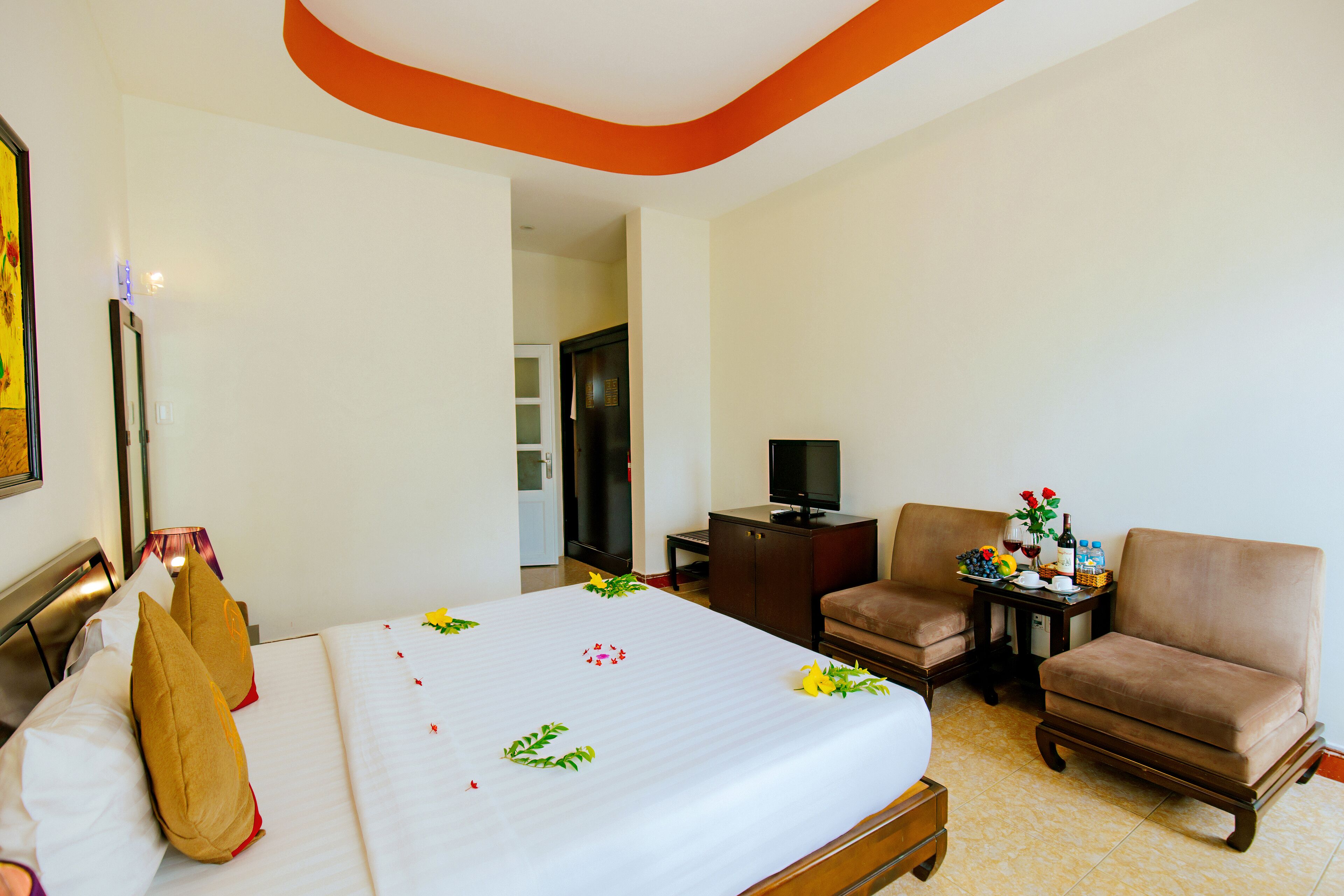 A hotel room with a bed, two armchairs, a television, and a small table with a vase of flowers.