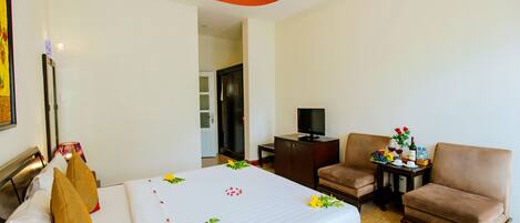 A hotel room with a bed, two armchairs, a television, and a small table with a vase of flowers.