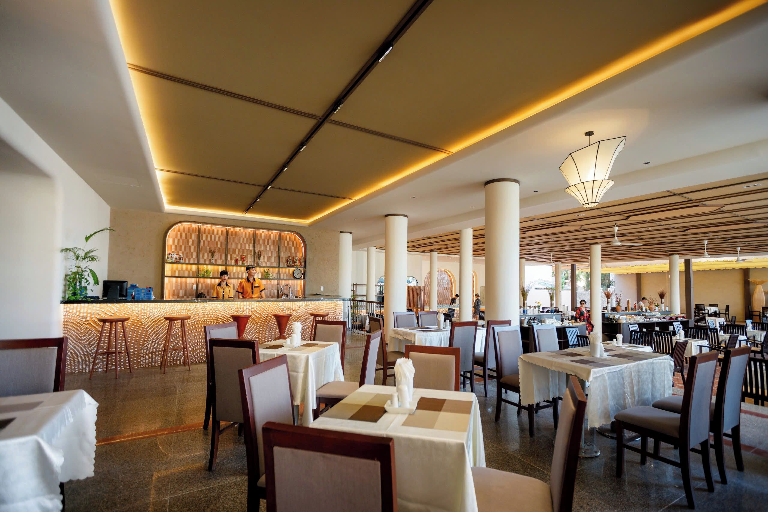 Un restaurante amplio con varias mesas y sillas, una zona de bar y un diseño de techo moderno.